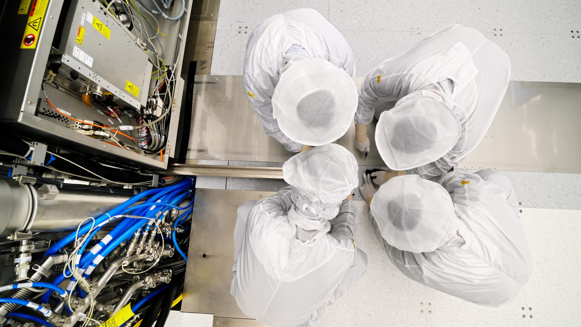 bird’s eye view of four cleanroom engineers working on the wafer stage of an ASML EUV system. bird’s eye view of four cleanroom engineers working on the wafer stage of an ASML EUV system.