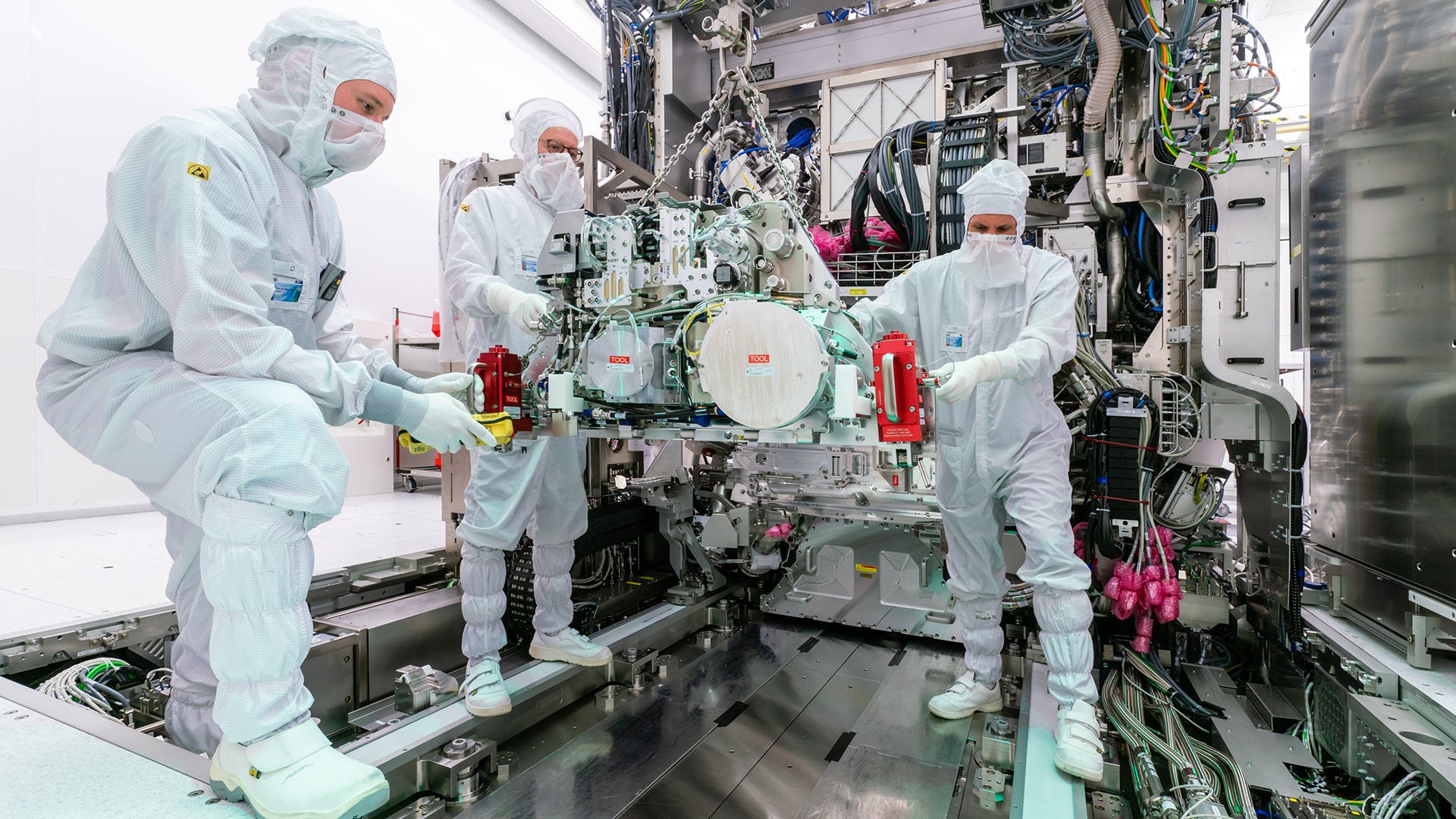 Three people in protective clothing working on a lithography machine Three people in protective clothing working on a lithography machine