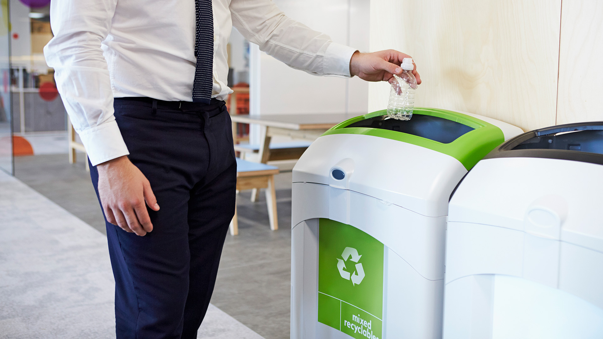 Partial view of an individual in business attire recycling waste into a green bin. Partial view of an individual in business attire recycling waste into a green bin.