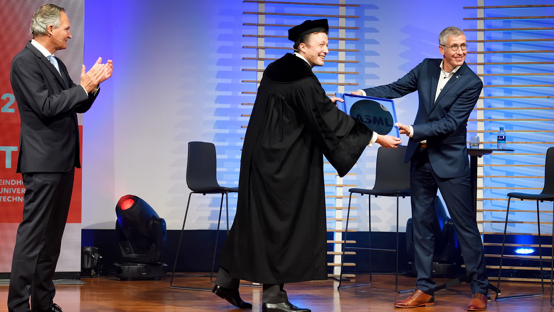 ASML vice president Frank Schuurmans symbolically hands over a present to TU/e president Robert-Jan Smits and TU/e professor Martijn Heck, scientific director of the Eindhoven Hendrik Casimir Institute.