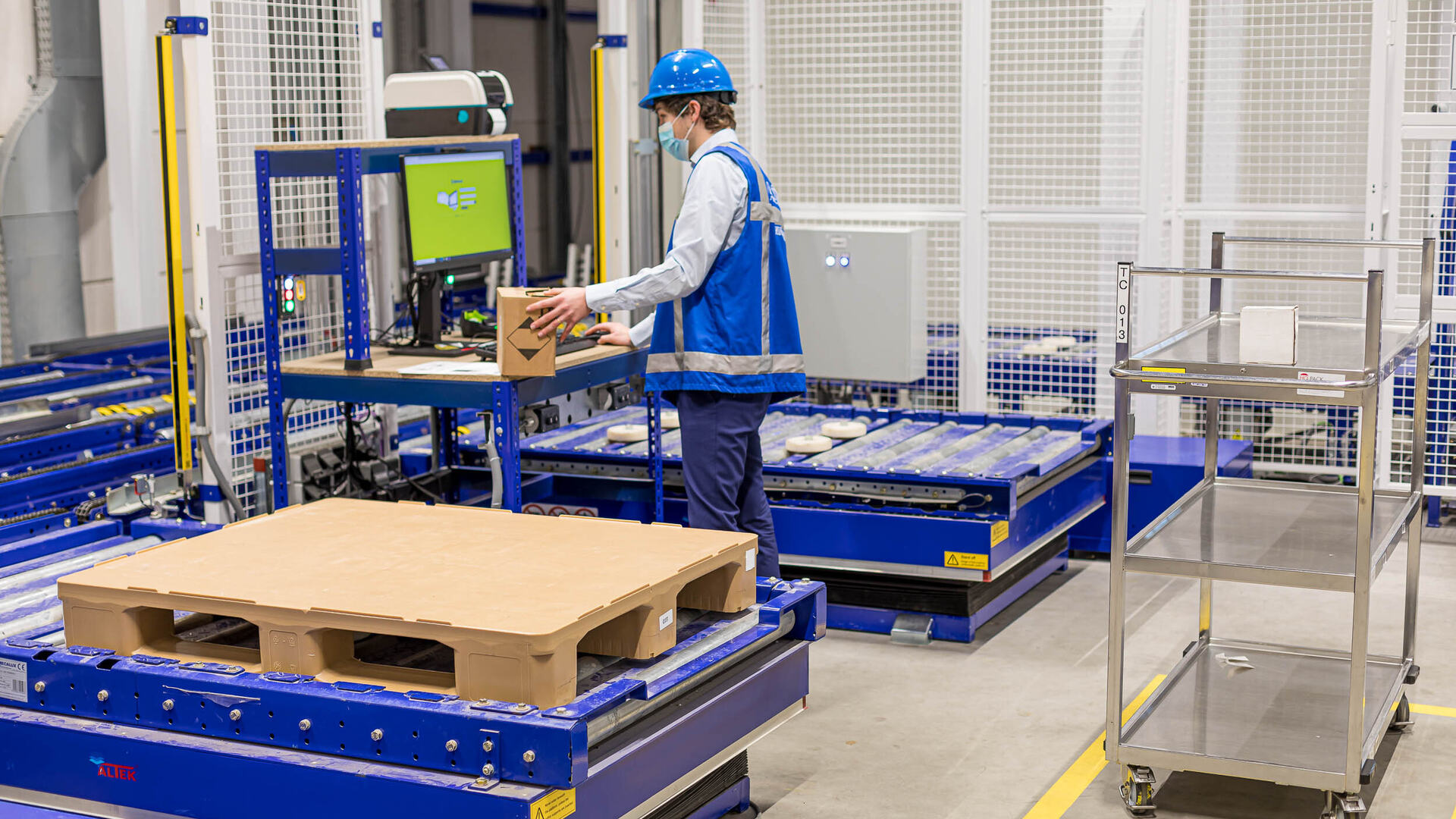 An employee wearing a blue safety vest and blue hardhat scans a box in a warehouse.