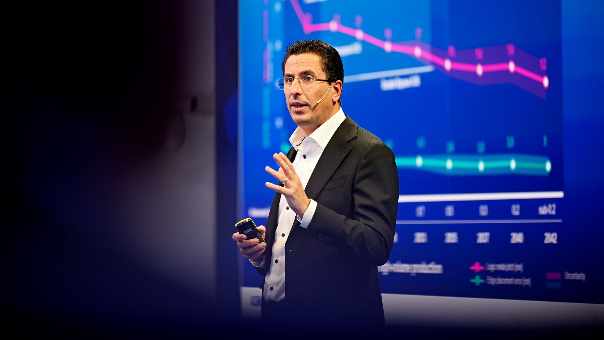 ASML CTO Marco Pieters speaks on stage while standing in front of a blue screen showing a graph. ASML CTO Marco Pieters speaks on stage while standing in front of a blue screen showing a graph.